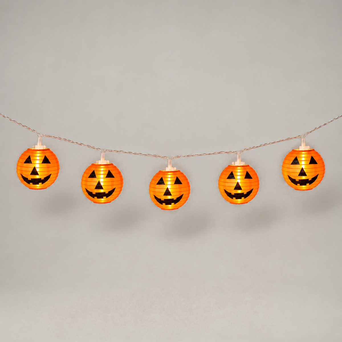 Five lit orange jack-o'-lantern lanterns hanging from clear wire in a gentle swag on a grey background