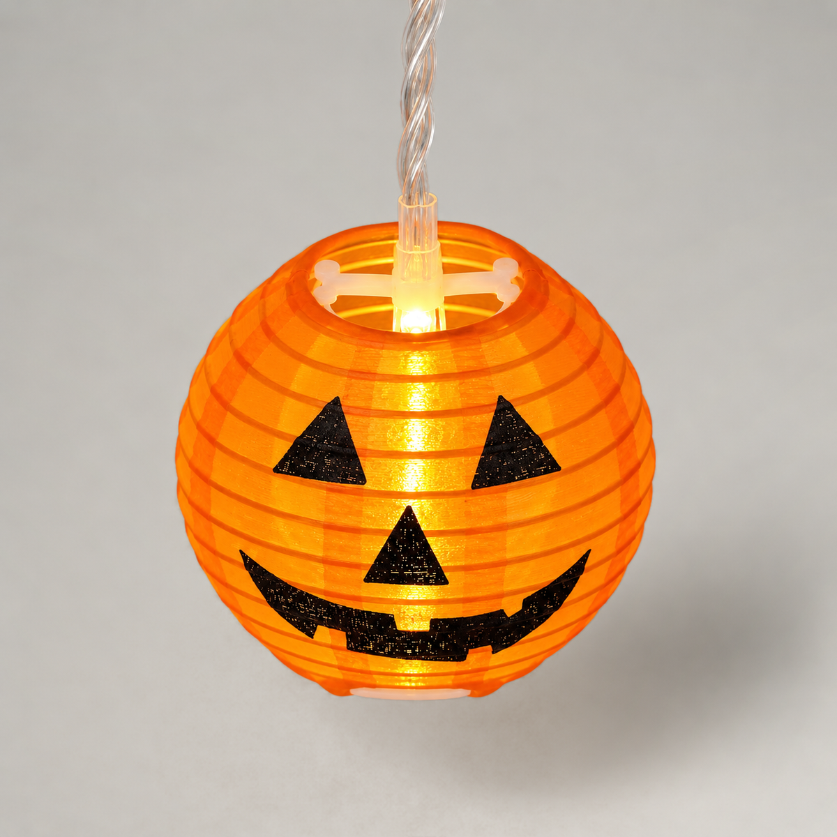 One lit orange ribbed lantern with a black jack-o'-lantern face, seen from slightly above to show the white spreader and LED in its open top