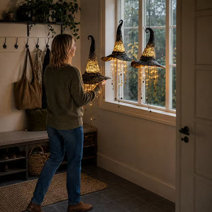 Woman hanging a witch hat light with glowing star strands beside a hallway window, two more hats in the window