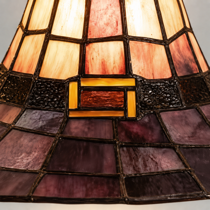 Close-up of the lamp's near-black band and flat amber buckle between glowing cream and rose panels and the plum brim