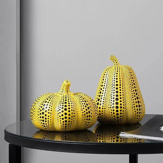 Small yellow pumpkin and pear sculptures covered in black polka dots on a round black glass side table