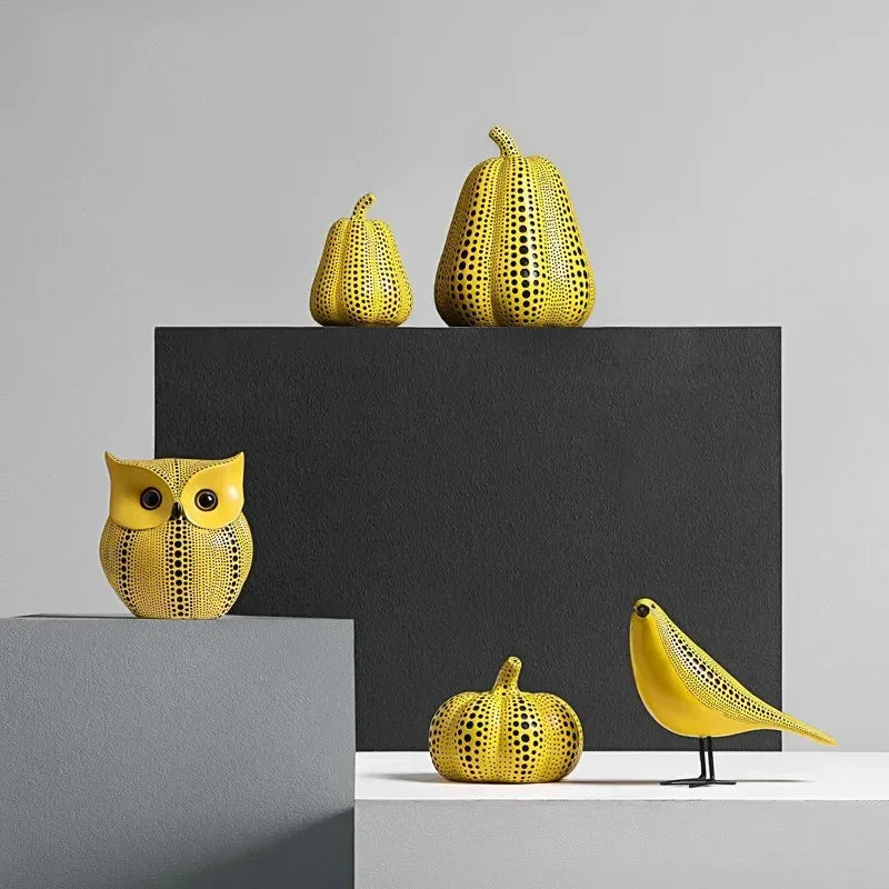 Polka dot owl, small and large pear, pumpkin and bird sculptures in yellow with black dots, grouped on gray, black and white display blocks