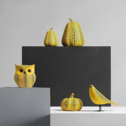 Polka dot owl, small and large pear, pumpkin and bird sculptures in yellow with black dots, grouped on gray, black and white display blocks