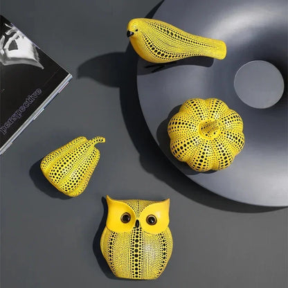 Polka dot bird, pumpkin, pear and owl sculptures in yellow and black, seen from above on a dark gray surface