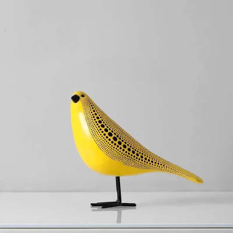 Bird polka dot sculpture in profile, smooth yellow breast, dotted back and long tail, standing on thin black legs