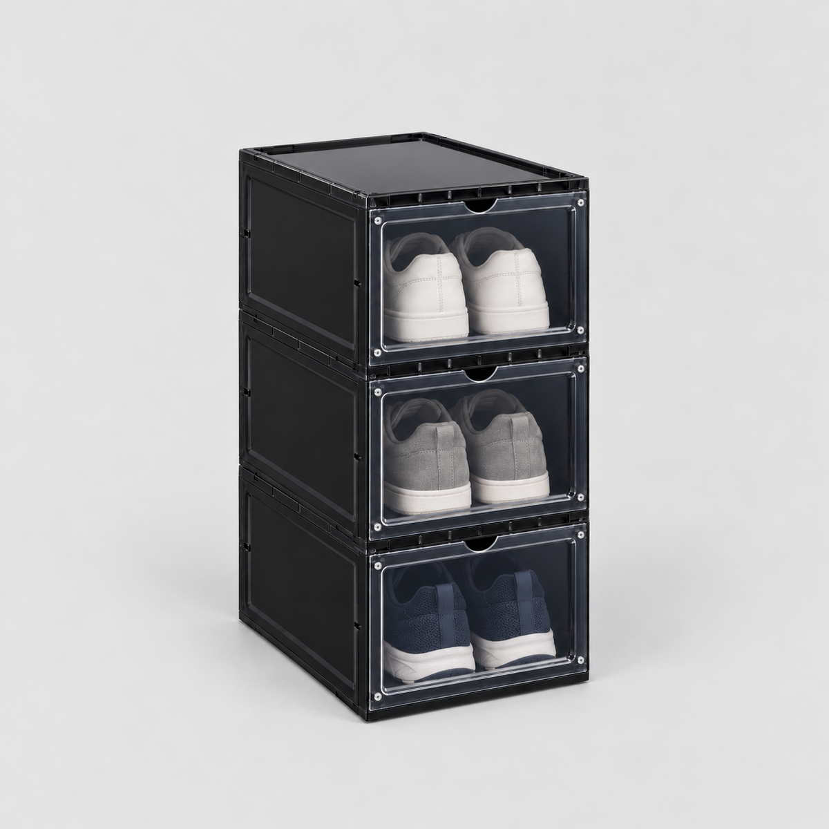 Set of three black drop front shoe boxes stacked in one column, a pair of sneakers in each, on a plain light grey background