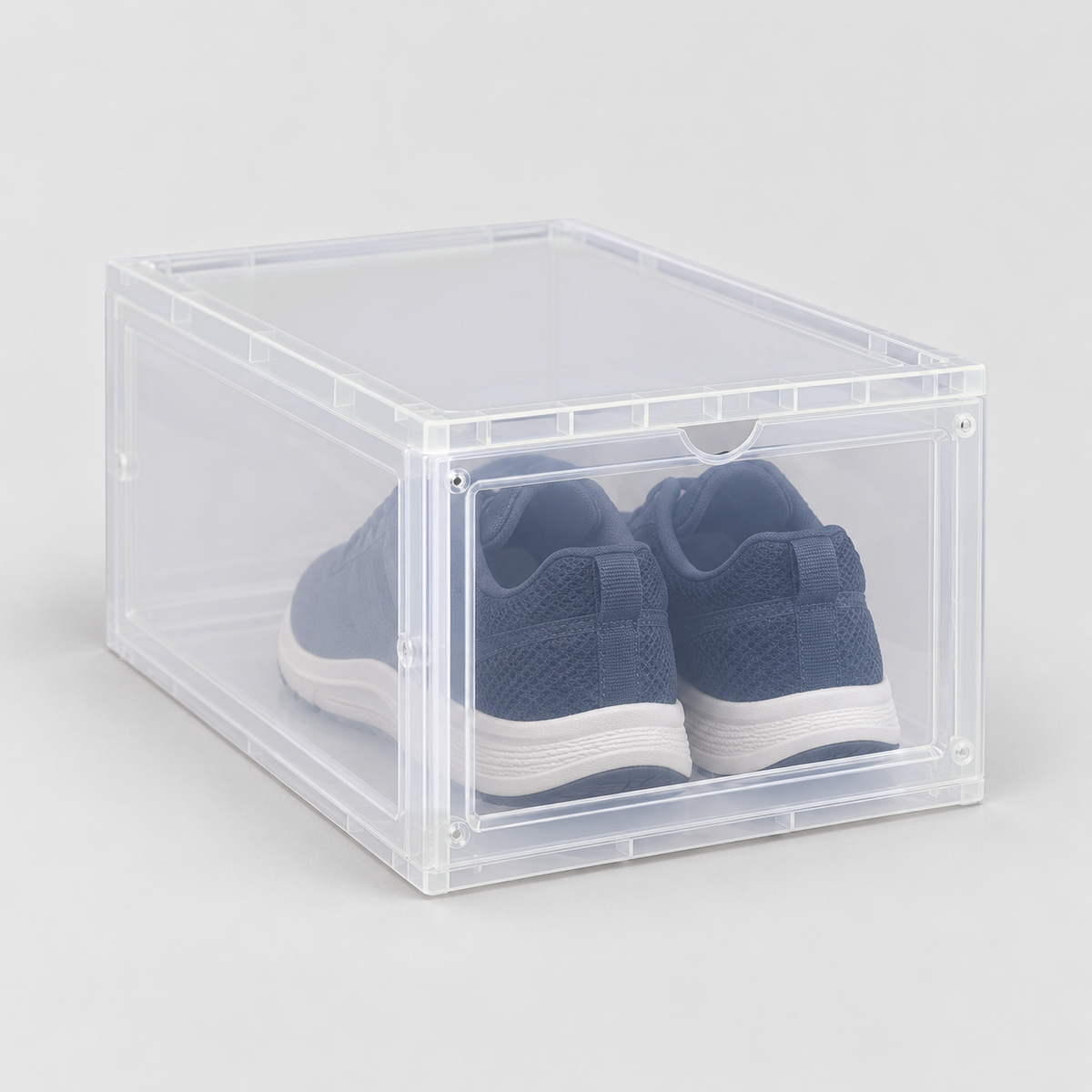Translucent drop front shoe box with navy running shoes inside, on a plain light grey background