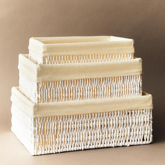 Three woven storage bins in small, medium and large, stacked one inside the next, white weave with a beige fabric liner folded over each rim