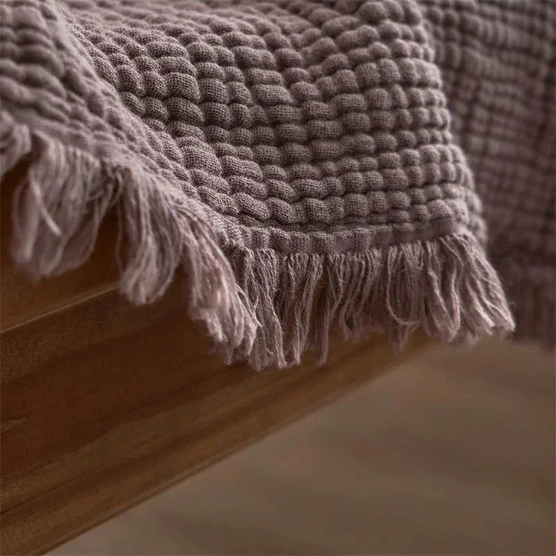 A close view of the small rounded puckers in mauve cotton gauze and the loose fringe along one corner.