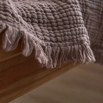 A close view of the small rounded puckers in mauve cotton gauze and the loose fringe along one corner.