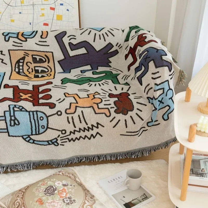 The doodle throw blanket spread over a couch seat in a bright living room beside a white side table and lamp.