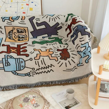 The doodle throw blanket spread over a couch seat in a bright living room beside a white side table and lamp.