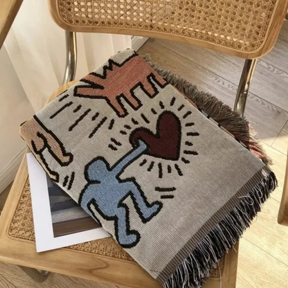 The throw blanket folded on a rattan chair, showing a blue figure holding a red heart.