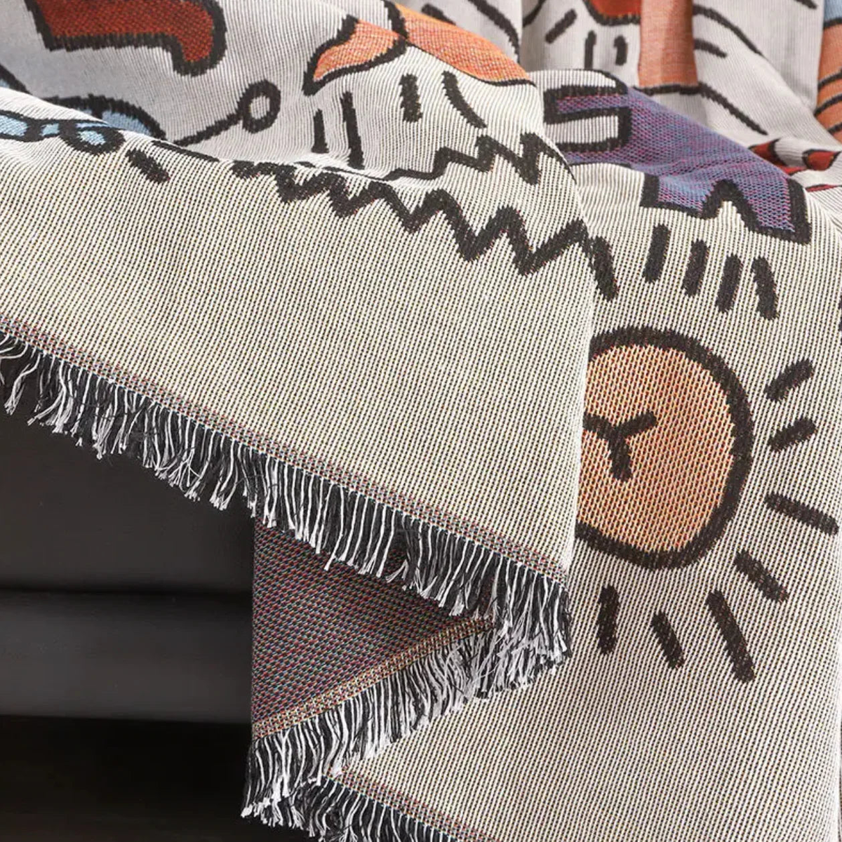 A fringed edge of the throw hanging down, with a corner turned to show the flecked reverse.