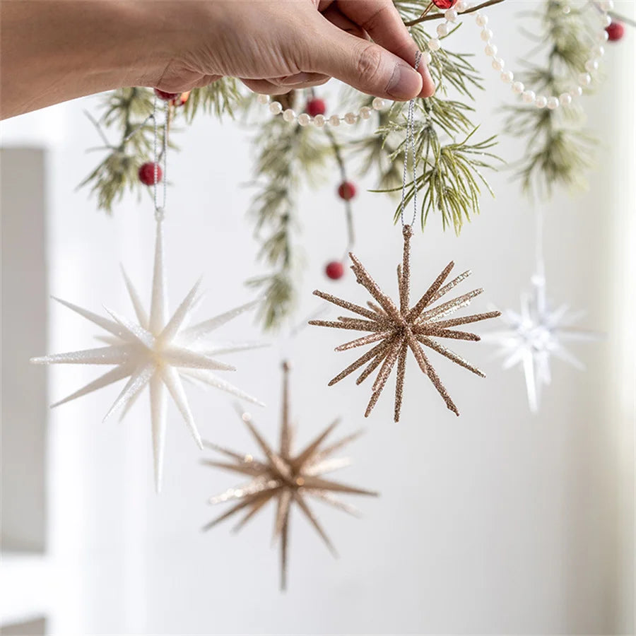 A hand hanging white, champagne and clear starburst ornaments on a pine garland