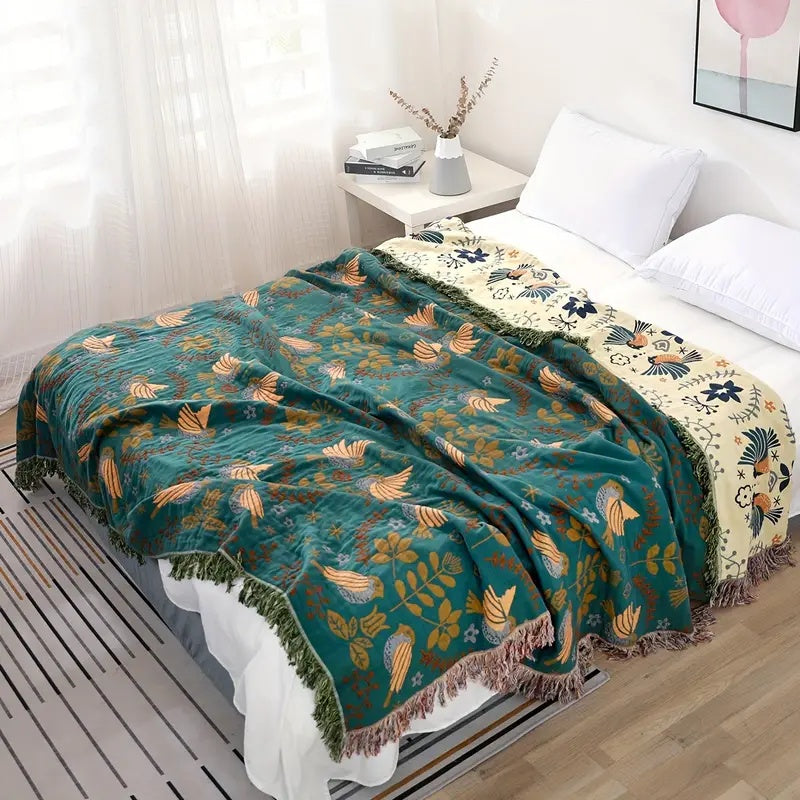 The teal bird throw over a bed seen from above, with the cream side turned back at the head of the bed