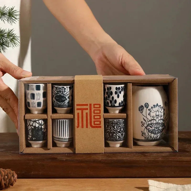 The sake set held up in its kraft box, cups on the left, decanter on the right, a sleeve round the middle.