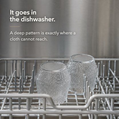Two hammered whiskey tumblers standing upside down on a dishwasher rack after a wash