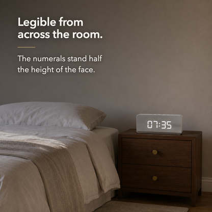 The mirror alarm clock seen from across a room, the large white digits still clearly readable at a distance
