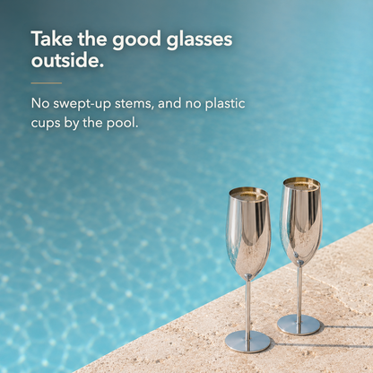 Two silver stainless steel champagne flutes filled with champagne standing on a stone pool edge