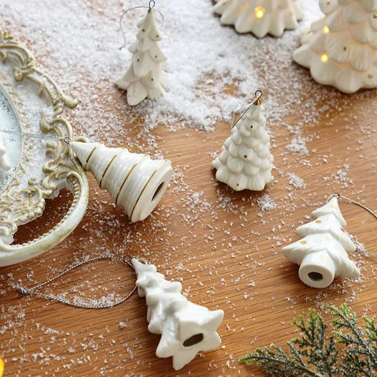White ceramic tree ornaments laid on a wooden table with artificial snow, two on their sides showing their open bases