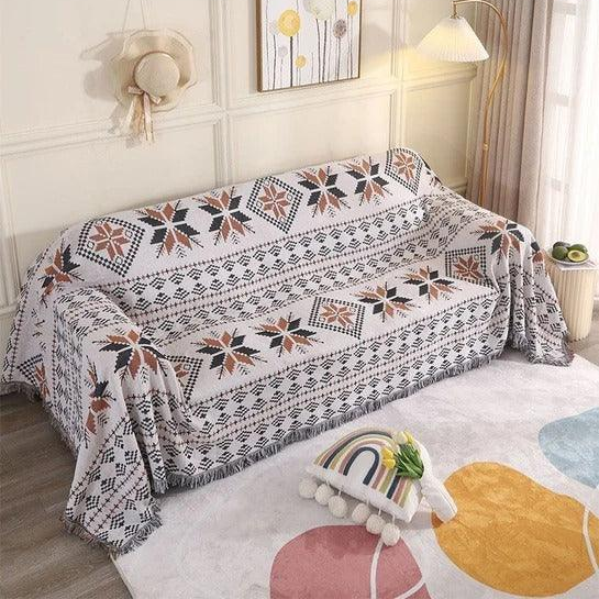 A cream jacquard throw with rows of rust and black stars, covering a whole couch in a bright living room