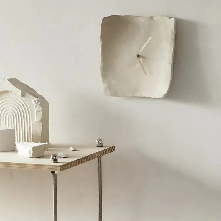 White crumpled resin wall clock on a pale wall above a plywood side table with plaster ornaments