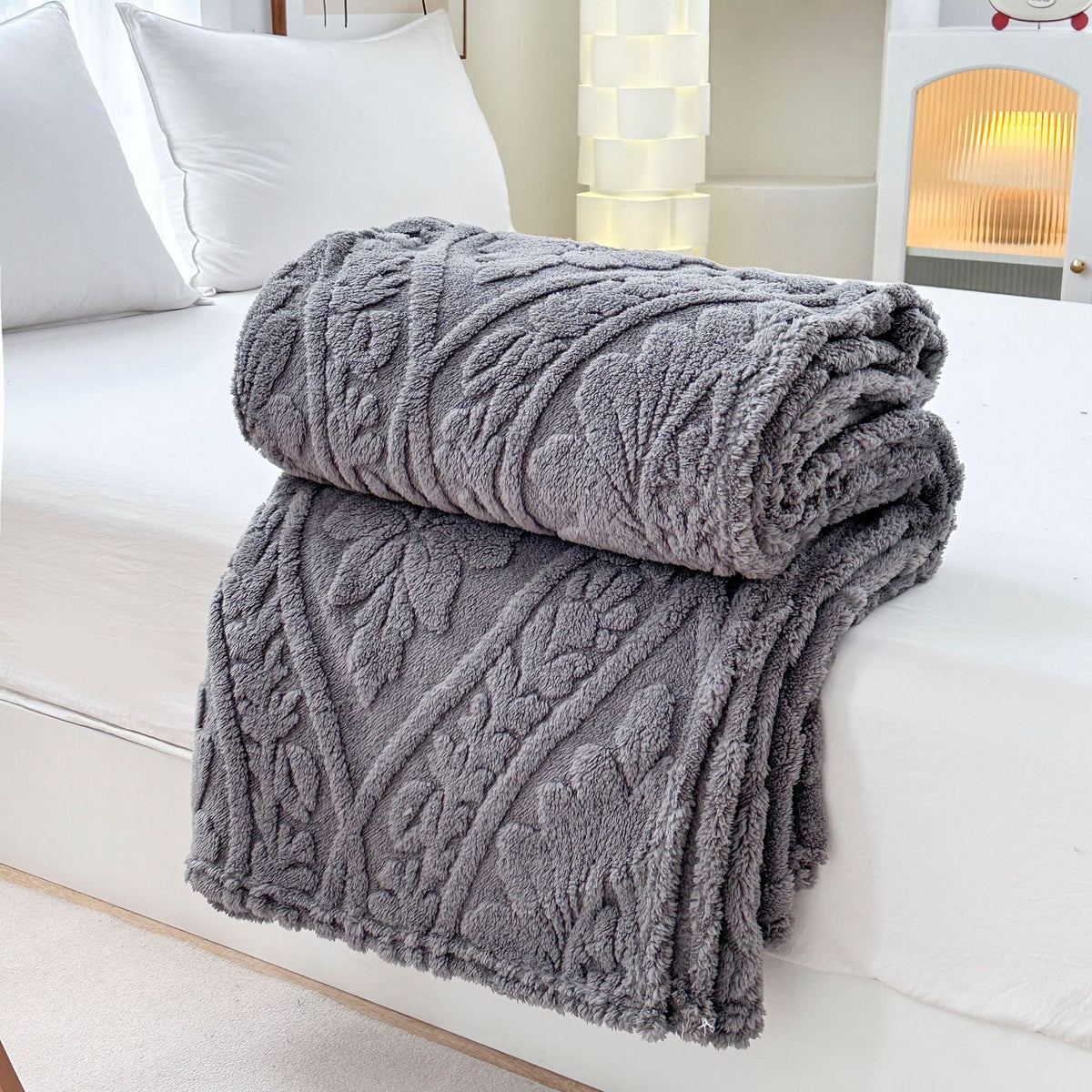 Gray embossed fleece blanket folded and rolled at the edge of a bed