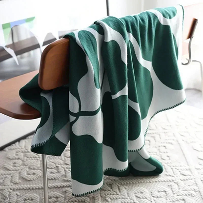A green and off-white knit throw blanket with an abstract pattern hung over the back of a wooden bench.