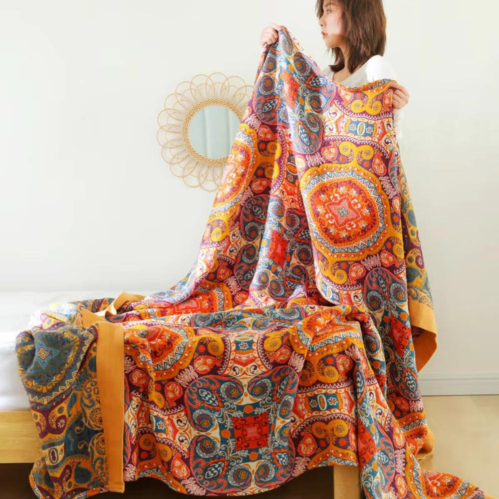 Throw blanket held up at the foot of a bed, showing both patterned faces and the mustard border
