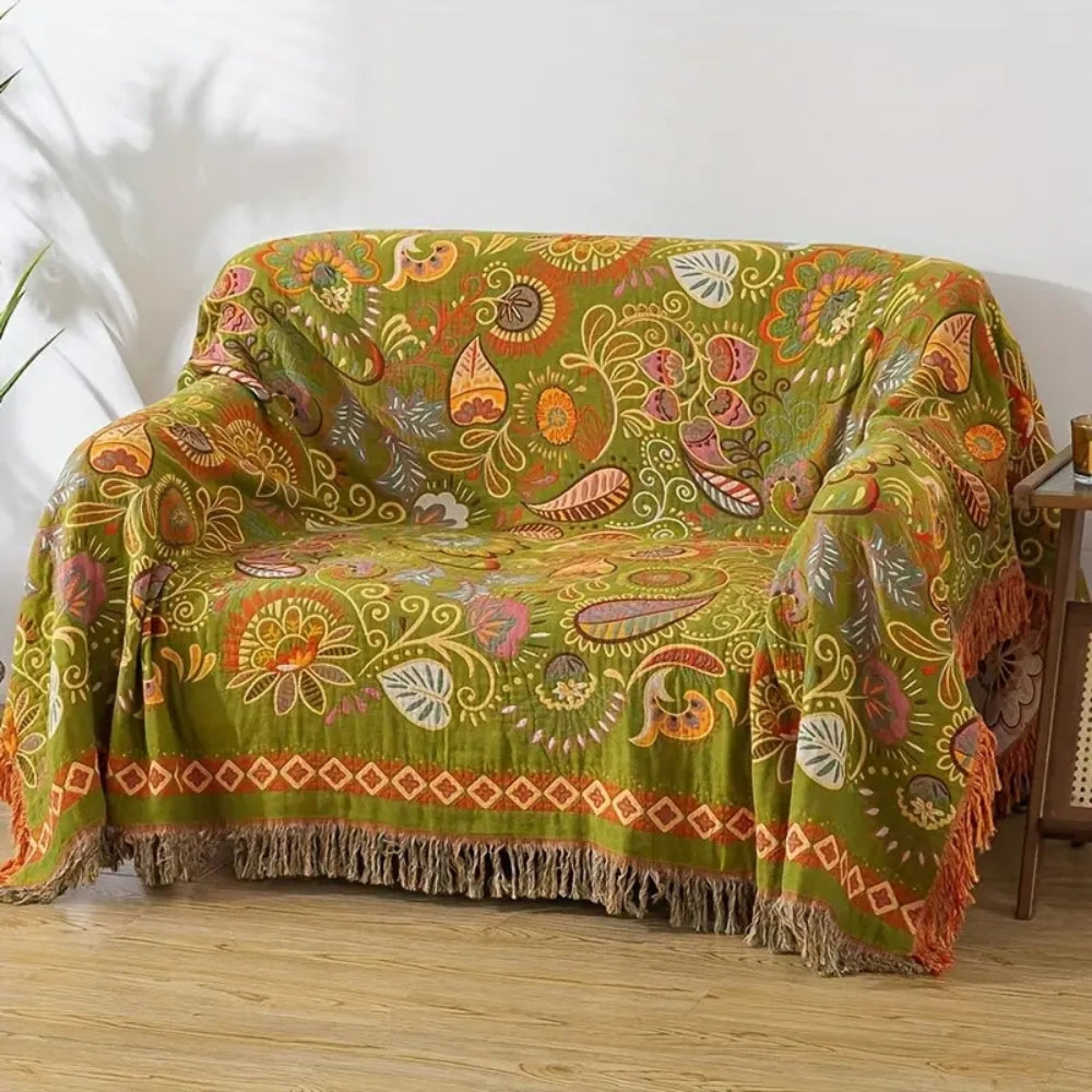 The olive side of the reversible throw draped over a loveseat, patterned with orange, pink and pale leaves and paisleys and edged with tassels