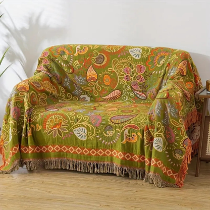 The olive side of the reversible throw draped over a loveseat, patterned with orange, pink and pale leaves and paisleys and edged with tassels