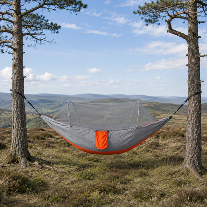 Orange ultralight camping hammock, grey with orange trim, on a hillside clearing
