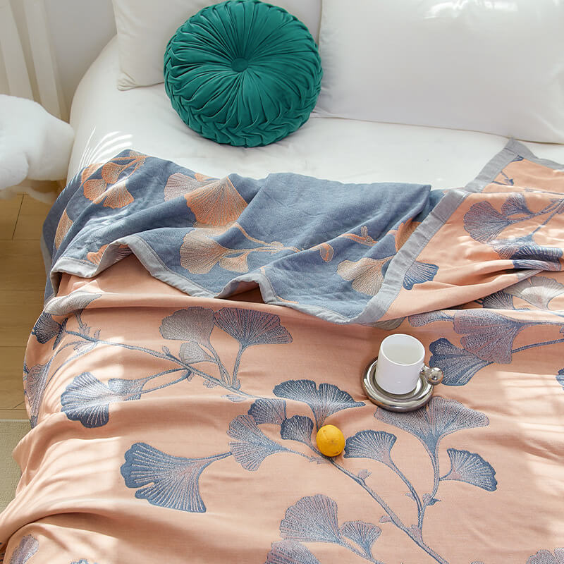 Peach ginkgo leaf quilt on a white bed beside a round green cushion, its corner turned back to show the slate reverse