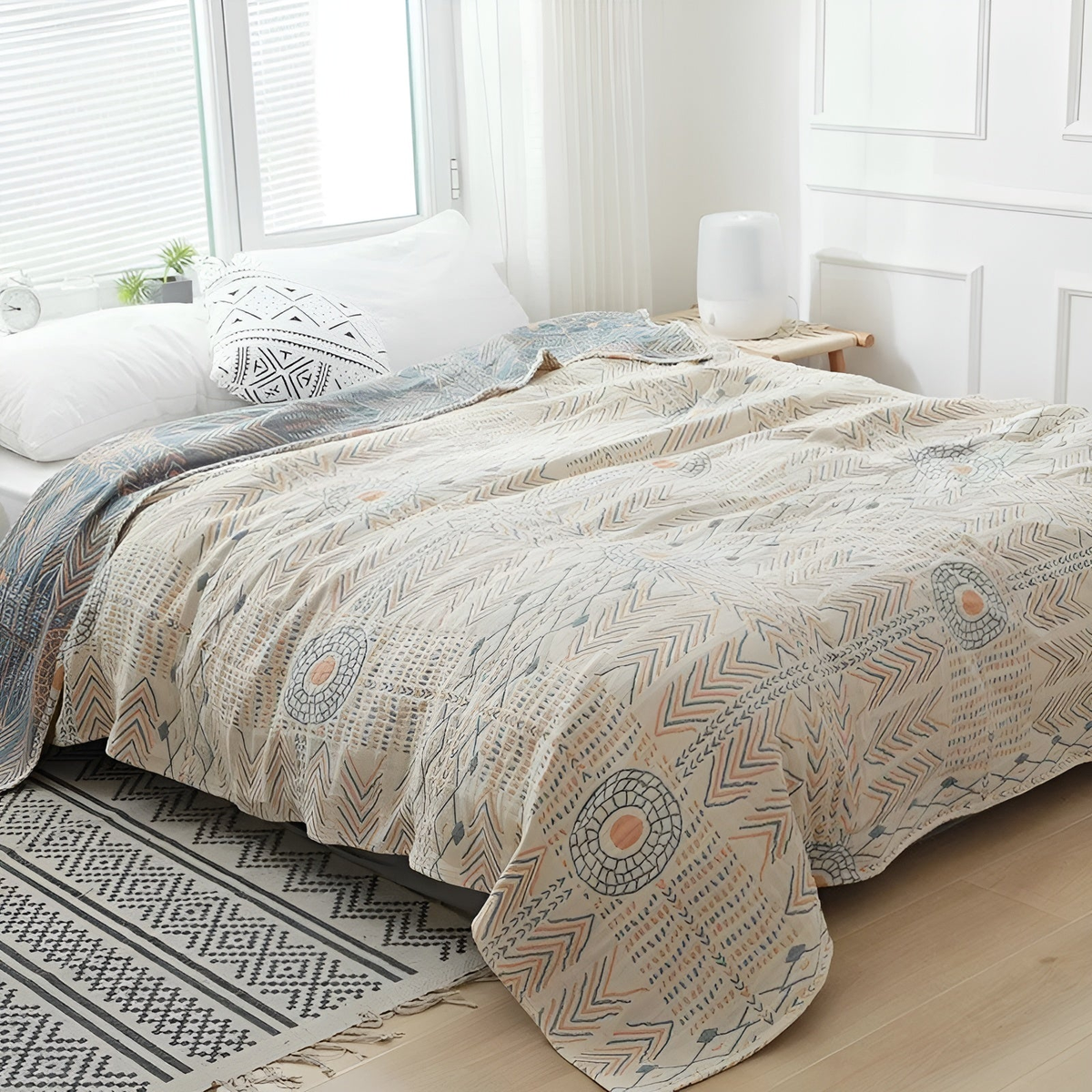 Cotton muslin blanket spread over a made bed, sun rings and chevrons in blue and orange, reverse folded back at the pillows