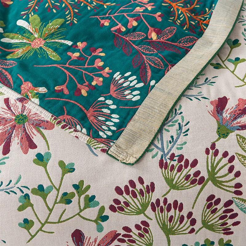 A corner of the cream wildflower blanket flipped over to show its teal floral reverse and oatmeal striped band