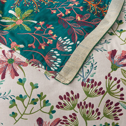 A corner of the cream wildflower blanket flipped over to show its teal floral reverse and oatmeal striped band