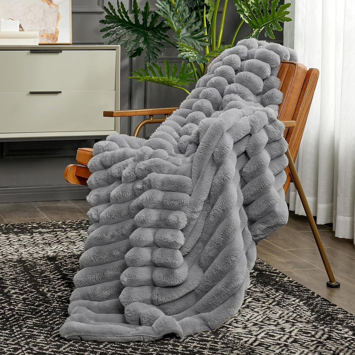 A gray ribbed faux fur throw hanging over a wood and leather armchair, its ribs running down onto a black and white rug.