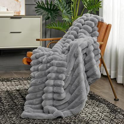 A gray ribbed faux fur throw hanging over a wood and leather armchair, its ribs running down onto a black and white rug.