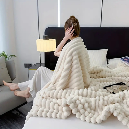 A woman sitting up in bed, seen from behind, with a cream ribbed faux fur throw around her shoulders and over the bed.