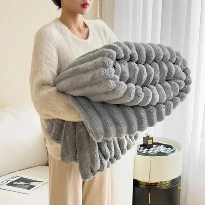 A woman in an off-white sweater carrying a folded gray ribbed faux fur throw blanket.
