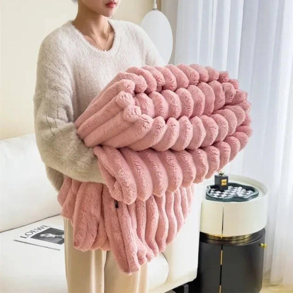 A woman in an off-white sweater carrying a folded pink ribbed faux fur throw blanket.