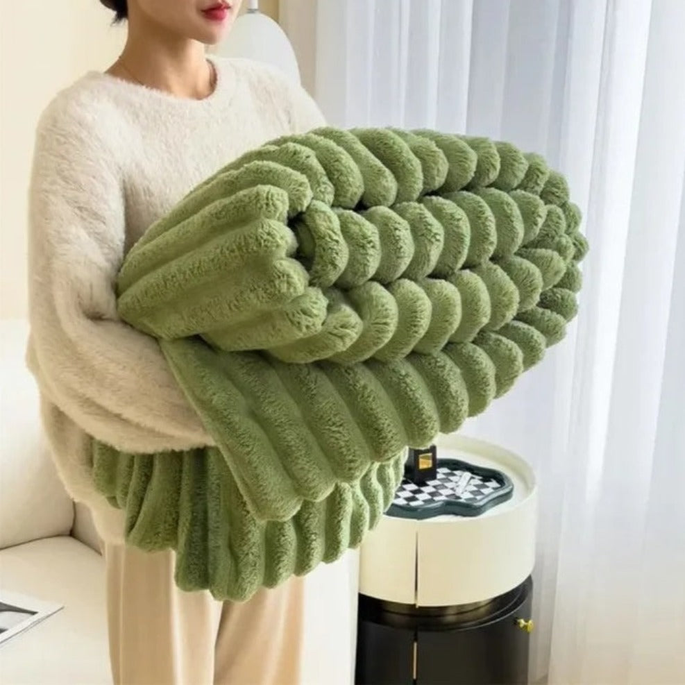 A woman in an off-white sweater carrying a folded green ribbed faux fur throw blanket.