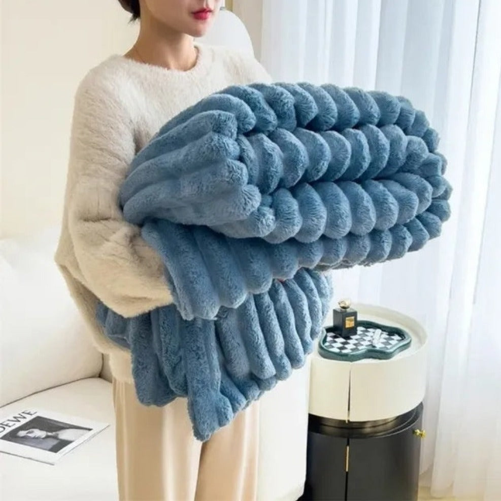 A woman in an off-white sweater carrying a folded blue ribbed faux fur throw blanket.