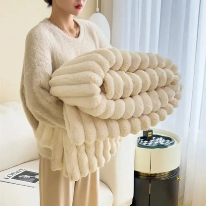 A woman in an off-white sweater carrying a folded cream ribbed faux fur throw blanket.