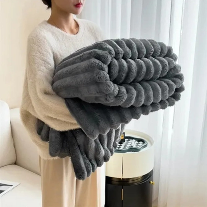 A woman in an off-white sweater carrying a folded charcoal ribbed faux fur throw blanket.