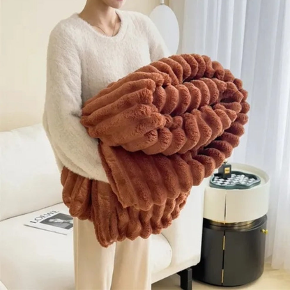 A woman in an off-white sweater carrying a folded terracotta ribbed faux fur throw blanket.