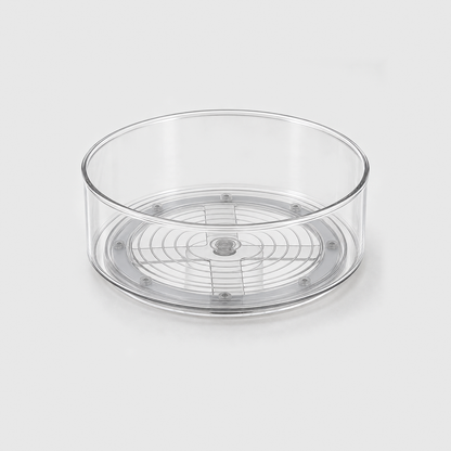 A clear round lazy Susan turntable, empty, on a light grey background, with its grey turning base visible through the clear floor.