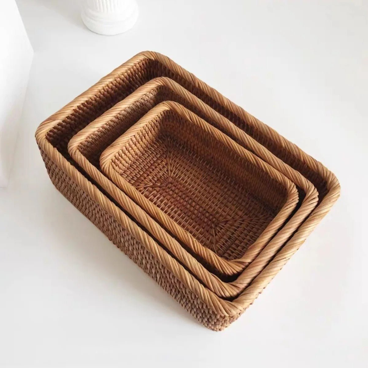 Three rattan storage baskets nested one inside the next on a white surface