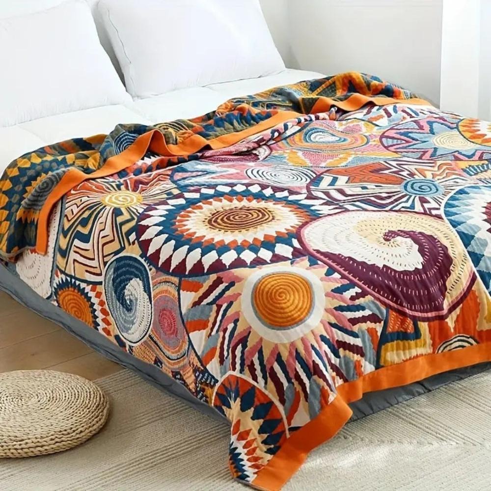 Sunburst cotton blanket spread over a bed, orange suns and burgundy shells on cream inside a wide orange border